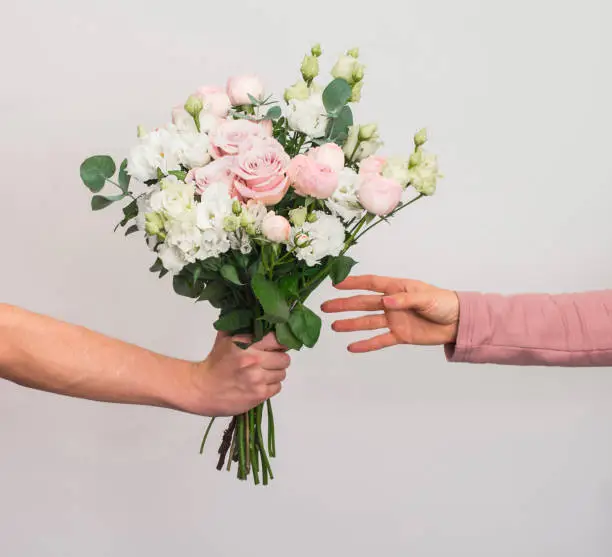 Photo of Flowers delivery concept. Hand giving pastel flowers bouquet to woman on grey background.