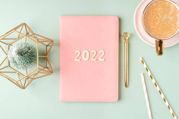 istock Top view Desktop Christmas pink notepad with 2022 letters text. Flat lay on green mint table background with planner, cup of coffee, candle, Christmas decoration, notebook and stationery 1357509724