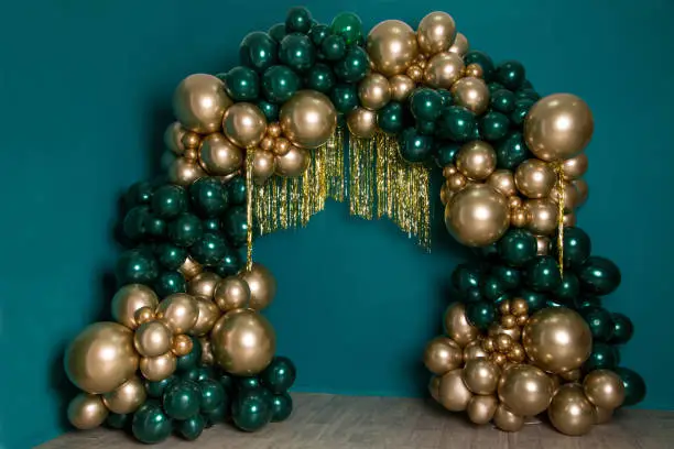 Arch of dark green and gold balloons on a green background