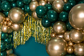 istock Arch of dark green and gold balloons on a green background 1357514307