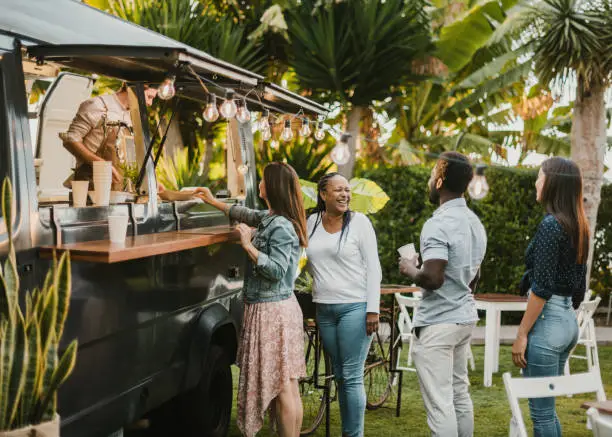 Happy black woman smiling and chatting with diverse friends while standing in queue near food truck in park on summer day