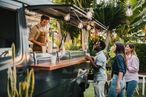Multiracial friends making order to seller in food truck Multiethnic friends standing in queue and ordering takeaway dishes from man in apron working in food truck in summer in park street food stock pictures, royalty-free photos & images