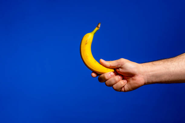 la mano tiene la banana. isolato su sfondo blu. alfa. - men banana holding cut out foto e immagini stock