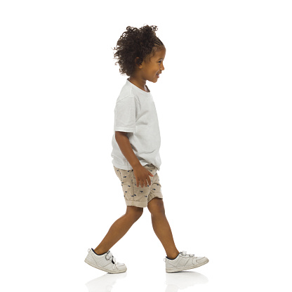 Sneaking happy little black boy. Side view. Full length studio shot isolated on white.