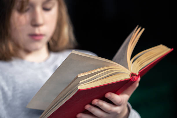 istock Serious little girl reading a book, blurred background. 1357520127