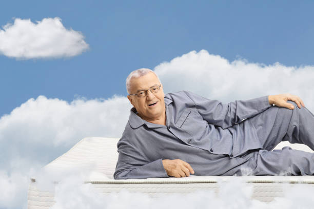 hombre maduro en pijama acostado en un colchón y flotando en el cielo - colchón para personas mayores fotografías e imágenes de stock