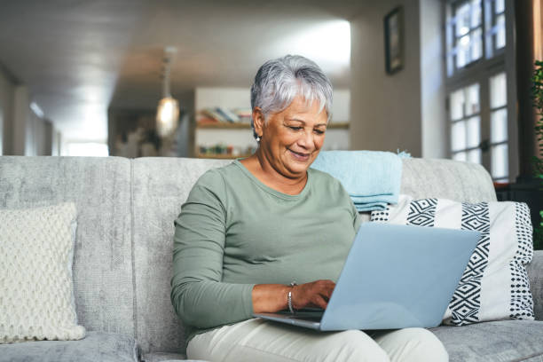 shot of a senior woman using a laptop on the sofa at home - laptop mature adult senior adult old imagens e fotografias de stock
