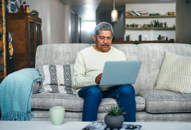 снимок пожилого мужчины, использующего дома ноутбук на диване - computer old men laptop стоковые фото и изображения