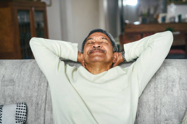 scatto di un uomo anziano felice che si rilassa sul divano di casa - inspirare foto e immagini stock