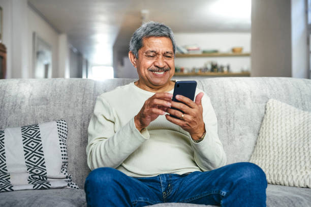 photo d’un homme âgé utilisant un smartphone sur le canapé à la maison - one mature man only photos et images de collection