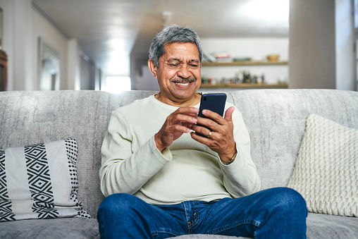 Shot of a senior man using a smartphone on the sofa at home