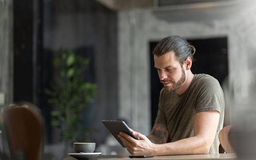 Attractive Beard man sitting using digital tablet at the coffee shop.