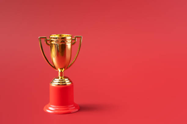 istock Gold color victory cup on red background 1357523437