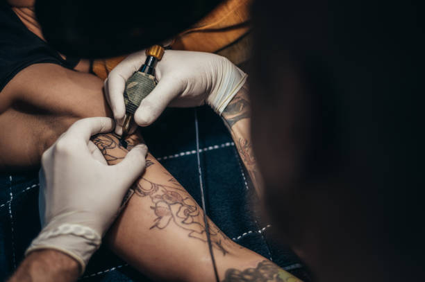 istock Tattoo artist hands in a white gloves holding a machine while creating a tattoo 1357523511
