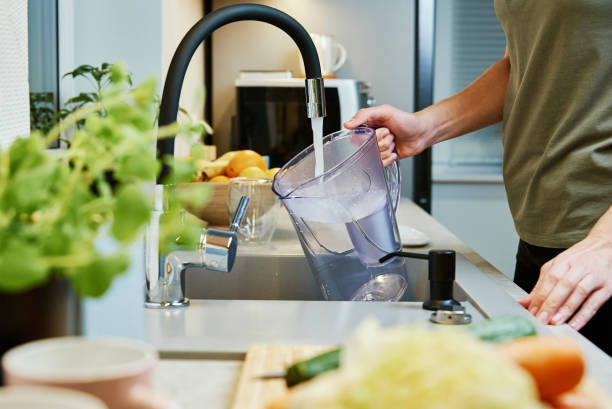 Woman pouring water filter jag Woman pouring water from faucet into water filter jug at the kitchen jug stock pictures, royalty-free photos & images