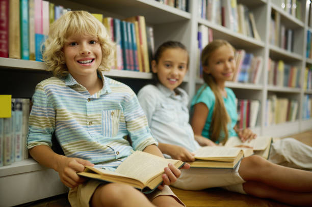istock Boy looking at camera sitting on floor with book 1357525383