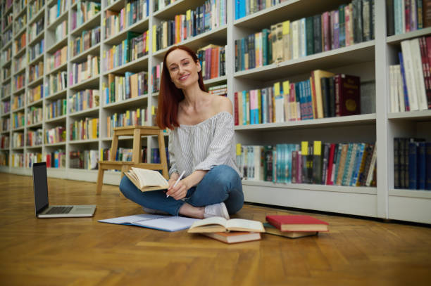 istock Woman sitting on floor in library studying 1357525580