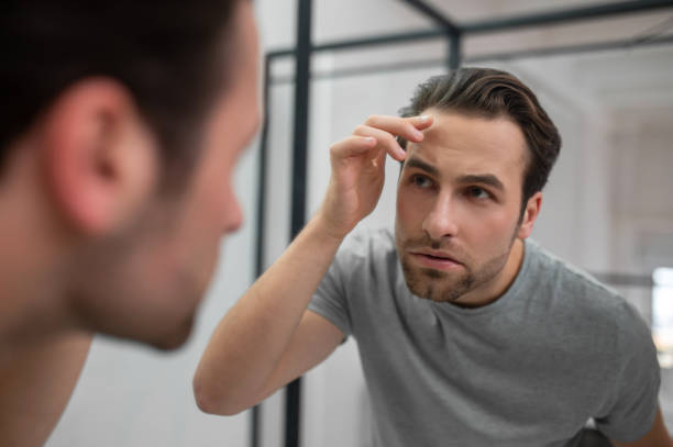 istock A young man in grey tshirt looking at his reflection in the mirror 1357526080