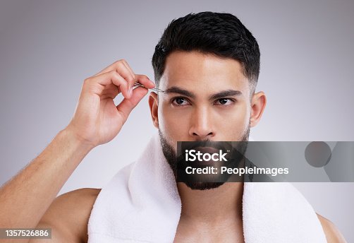 istock Shot of a young man tweezing his eyebrows against a studio background 1357526886