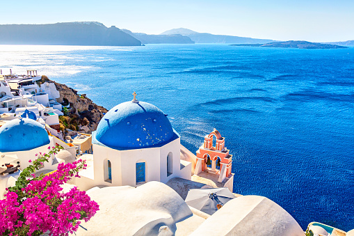 Famous Santorini iconic view. Blue domes and traditional white houses with bougainvillea flowers. Oia village, Santorini island, Greece