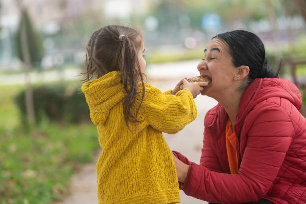 foto de madre e hija de 3,5 años comiendo pan en parque público - 35 40 years fotografías e imágenes de stock