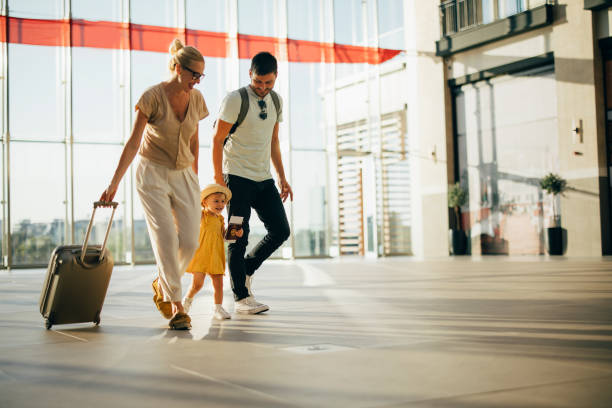 Loving Family Going on Holiday Together Cheerful smiling husband and his wife holding hands and walking with their little girl and luggage at the airport. kid holding fathers hand stock pictures, royalty-free photos & images
