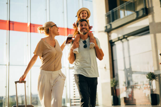 Excited Family Going on Vacation Together Cheerful husband carrying his cute daughter on shoulders while walking with his beautiful wife and luggage at the airport. airport stock pictures, royalty-free photos & images