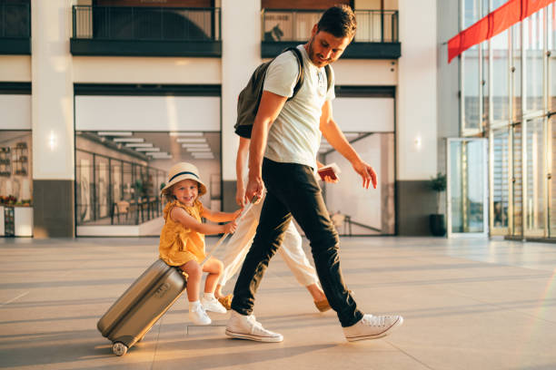 Young Family Having Fun Traveling Together Cheerful husband and his anonymous wife walking with their little girl sitting on luggage at the airport. passenger stock pictures, royalty-free photos & images