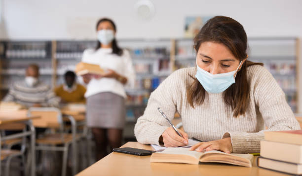 istock Young Latina in medical mask spending time in library 1357530326
