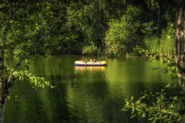 niños navegando en barco en el río entre exuberantes árboles de follaje en un soleado día de verano en el campo concepto de aventura infantil - child inflatable raft lake family fotografías e imágenes de stock