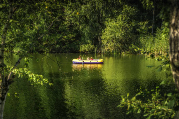 화창한 여름날, 시골 에서 모험 어린 시절의 라이프 스타일을위한 시골 개념에서 무성한 단풍 나무 사이에서 강에서 보트로 항해하는 아이들 - child inflatable raft lake family 뉴스 사진 이미지