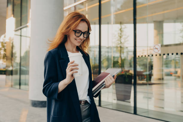 istock Smiling redhead woman corporate worker dressed in formal clothes drinks coffee 1357531139