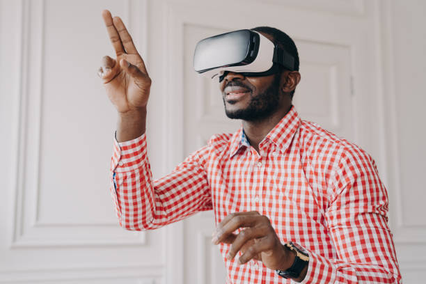 istock Impressed african ethnicity guy in VR headset glasses enjoying virtual reality online at work 1357531222