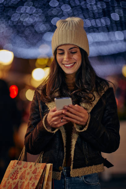 istock Smiling woman with woolen cap using cellphone outdoors in the city 1357532178