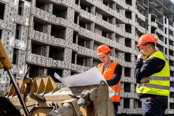 istock wonderful male workers in uniform and with helmets consider a construction plan on a grader 1357533216