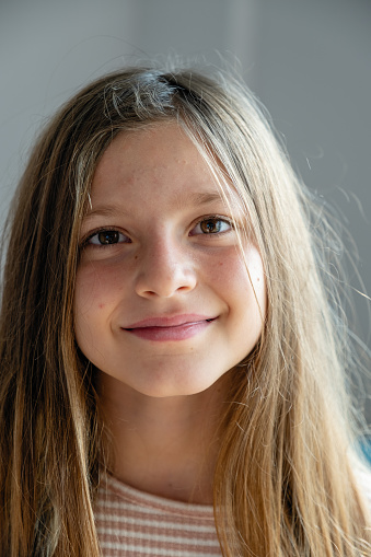 Portrait of a beautiful brunette girl looking at the camera and smiling, standing on the street against the backdrop of greenery on a summer day. Young curious child raises his eyes and lowered his head looks at the camera close-up outdoors. Face Eyes Contemplative Child.