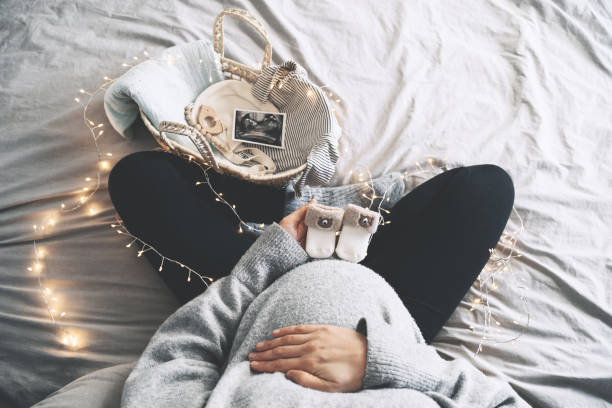 pregnant woman holding little baby socks near her belly. expectant mother preparing wicker basket with ultrasound image and stuff for newborn baby during pregnancy. - abdomen gynecological examination women loving imagens e fotografias de stock