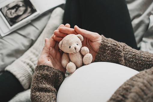 Mujer embarazada vientre con un pequeño oso de peluche. Imagen conceptual con símbolo de muchos significados para la futura madre durante el embarazo y su bebé por nacer. photo