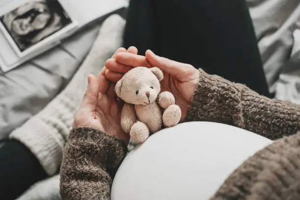 Photo of Woman pregnant belly with little teddy toy bear. Concept image with symbol of many meanings for expectant mother during pregnancy and her unborn baby.