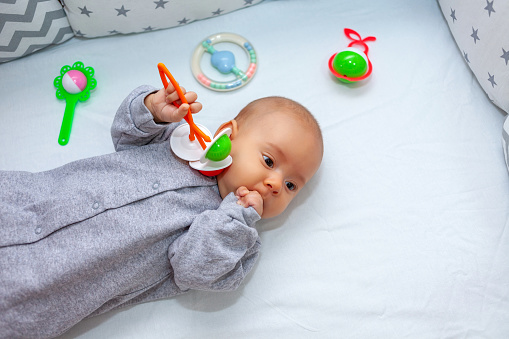 A child with a rattle in his hands lies on the crib. Top view