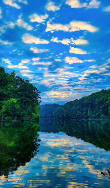 Large puffy cloud reflecting tree lined lake in the late morning stock photo