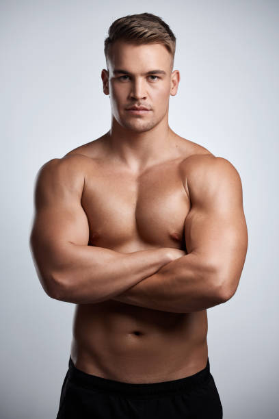 studio portrait of a muscular young man posing with his arms crossed against a grey background - sensuality men shirtless studio shot imagens e fotografias de stock