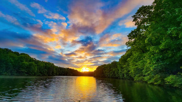 Glow of sunrise on partly clouded day over tree lined lake with reflection