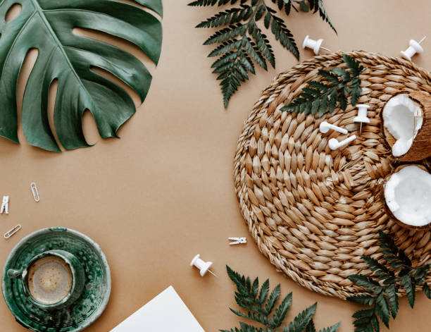 Natural flat lay with coffee cup, coconut, green monstera leaf on brown background. Space for text, blogger background, neutral colors, workspace