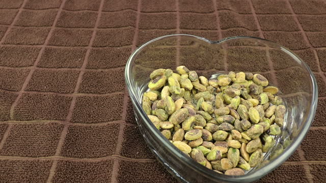 Person Pouring Pistachios from a Bowl to a Heart Shaped Dish