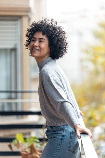 istock Beautiful woman posing while looking at camera standing in the balcony at home. 1357546721