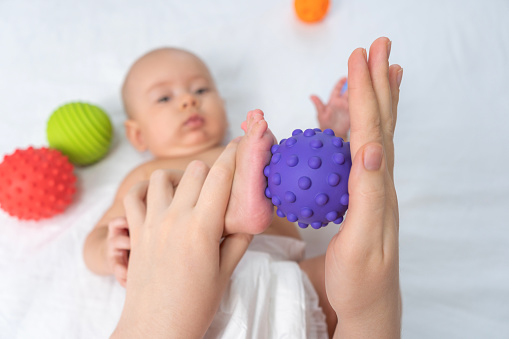 Mom gives baby foot massage with purple rubber ball. Selective focus
