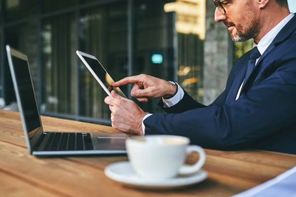 istock Closeup shot of a mature businessman using a digital tablet and laptop while working at a cafe in the city 1357548097