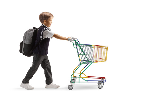 Full length profile shot of a schoolboy pushing a mini shopping cart isolated on white background
