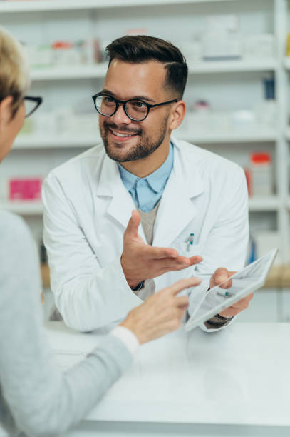 男性薬剤師がドラッグストアで薬を販売するシニア女性顧客へ - pharmacy pharmacist smiling pill ストックフォトと画像